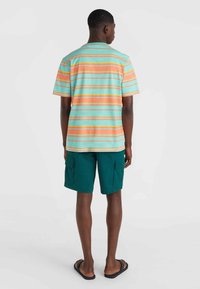 Chemise à manches courtes rayée dans des tons turquoise, orange et jaune. Associée à un short cargo vert. Le tissu semble léger, avec un design décontracté.