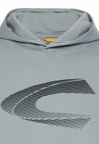 Hellgrauer Kapuzenpullover mit einem großen, stilisierten schwarzen Logo mit Linien, das ein lässiges und sportliches Design zeigt.