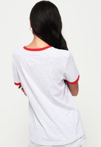 Weißes T-Shirt mit kurzen Ärmeln und rotem Besatz am Kragen und an den Ärmeln, mit einem schlichten Design und aus weichem, leichtem Stoff.