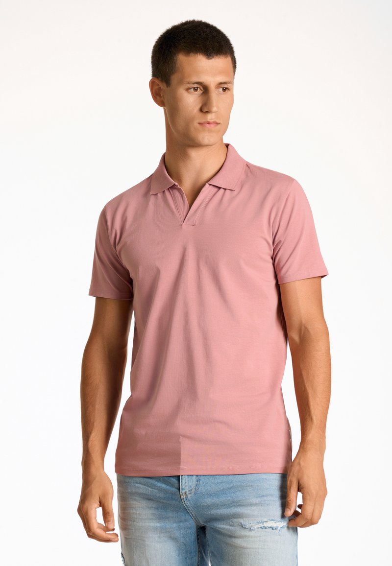 Rosa polo skjorta med klassisk krage och korta ärmar, tillverkad av ett texturerat tyg. Bärs med blekta blå jeans som visar en avslappnad passform.