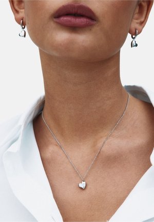 Srebrni uhani v obliki srca in ujemajoča se ogrlica na modelu, z nežno verižico in gladkimi, poliranimi površinami.