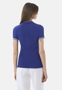 Koszulka polo w kobaltowym niebieskim kolorze, z krótkimi rękawami, białymi akcentami na kołnierzyku i mankietach, wykonana z gładkiego, elastycznego materiału; dopasowany krój.