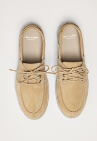 Beige Wildlederschuhe mit runder Zehenpartie, kontrastierenden Nähten und schwarzen Ösen. Die Schnürsenkel sind ordentlich gebunden und zeigen ein einfaches, klassisches Design.