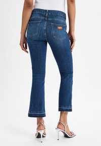 Jeans a zampa d'elefante in denim blu scuro con orlo grezzo, dotati di due tasche posteriori e una toppa in pelle con il marchio in vita.