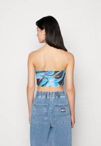 Top cropped sem mangas com padrão espiral azul e castanho, combinado com jeans de ganga claros de cintura alta, com cintura elástica e bolsos.
