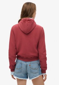 Felpa con cappuccio rossa corta con coulisse, polsini e orlo a coste, abbinata a shorts di denim sfrangiati con cuciture sulle tasche posteriori.