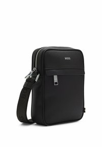 Svart axelväska med dragkedjestängning, tillverkad av texturerat material, med en framficka och en rem med logodetaljer. Silverfärgade detaljer.