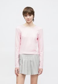 Ροζ μπλούζα με μακριά μανίκια από απαλό ύφασμα, συνδυασμένη με φούστα σε γκρι χρώμα με πιέτες. Απλός σχεδιασμός με στρογγυλή λαιμόκοψη και εφαρμοστή γραμμή.