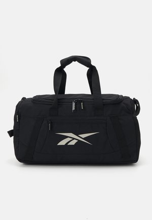 Čierna cestovná taška vyrobená z odolného materiálu, s dvoma hornými uchami, zipsovými priehradkami a výrazným strieborným logom Reebok na boku.