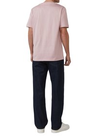 Helles rosa Baumwoll-T-Shirt mit kurzen Ärmeln, rundem Ausschnitt und lockerer Passform, kombiniert mit dunkelblauen Denim-Hosen und weißen Sneakers.