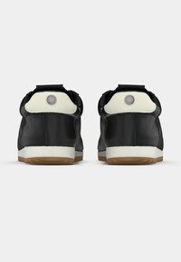 Μαύρα αθλητικά παπούτσια από δέρμα με λευκές λεπτομέρειες, επενδυμένη φτέρνα, στρογγυλό λογότυπο και λαστιχένια σόλα. Συμπαγής σχεδιασμός με ραφές στις πλευρές.