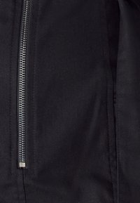 Černá bunda se stříbrným zipem uprostřed, vyrobená z hladkého textilního materiálu s jemnou texturou a čistými švy.