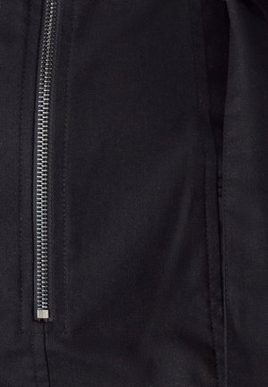 Juoda striukė su sidabriniu užtrauktuku centre, pagaminta iš lygaus tekstilės audinio su subtilia tekstūra ir švariais siuvimo akcentais.