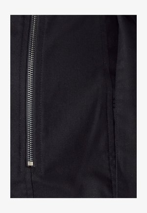 Juoda striukė su sidabriniu užtrauktuku centre, pagaminta iš lygaus tekstilės audinio su subtilia tekstūra ir švariais siuvimo akcentais.