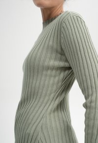 Rippstrick, langärmliger Pullover aus leicht grünem Strick. Mit Rundhalsausschnitt und taillierter Silhouette. Texturiertes Muster über das gesamte Stück.