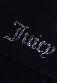 Λέξη "Juicy" σε στυλιζαρισμένη μορφή, σχηματισμένη από μικρά ασημένια στρας σε μαύρο ύφασμα, δημιουργώντας ένα λαμπερό διακοσμητικό σχέδιο κειμένου.