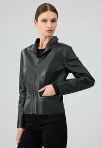 Giubbotto di pelle nera con colletto rialzato, due tasche frontali con zip e design aderente. Texture liscia con dettagli di cucitura minimi.