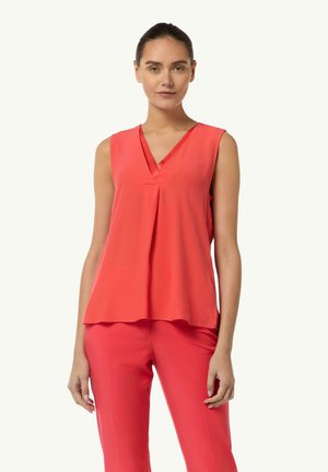 Sleeveless coral blouse with a V-neck and pleat detail. The fabric is smooth and lightweight, creating a flowing silhouette.
