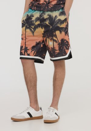 Pantaloni corti a rete multicolori con design a tramonto con palme, bordo nero e tasche laterali. Abbinati a sneakers bianche e dettagli neri.
