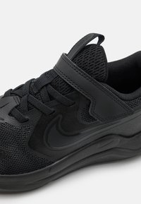 Chaussure de sport noire avec un dessus en maille, des accents texturés, un col rembourré, un système de laçage et de velcro, et une semelle rembourrée.