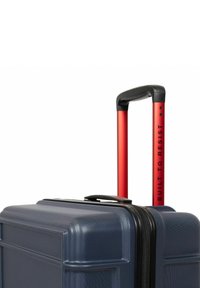 Hard-shell suitcase in navy blue with textured surface, black zipper, and red telescopic handle marked "BUILT TO RESIST."