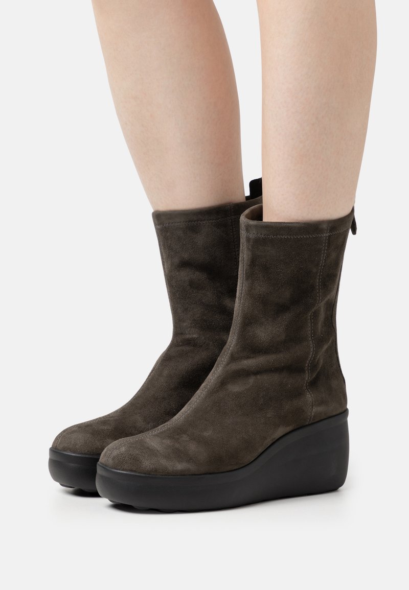 Bottines en suede marron foncé avec un talon en coin, texture douce et une languette à l'arrière pour un enfilage facile. Design minimaliste avec des lignes épurées.