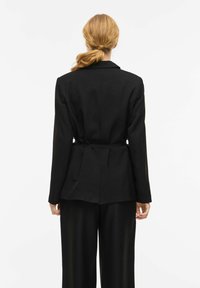 Blazer nero su misura con maniche lunghe, spalle strutturate, vita stretta e schiena dritta. Tessuto liscio con dettagli minimi.