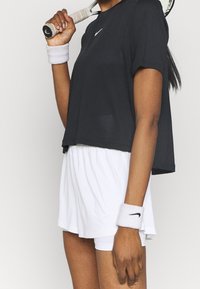 Camiseta atlética negra de manga corta con material texturizado y logo de Nike en blanco, combinada con pantalones cortos blancos y muñequeras con el logo de Nike.