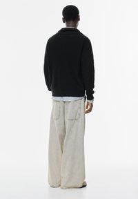 Fekete kötött pulóver ribbed textúrával, oversized világosszürke farmernadrággal, melyen hátsó zsebek találhatók. A modell hátulról van látható.
