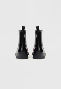 Bottines en cuir noir avec des panneaux élastiques sur les côtés, des languettes de tirage et des semelles en caoutchouc texturé, affichant un design élégant et moderne.
