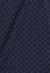 Granatowy materiał z fakturowaną powierzchnią, na której widoczny jest biały wzór diamentowy stworzony z małych kropek równomiernie rozmieszczonych na całej powierzchni.