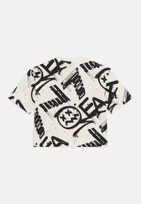 Korte ermer, cropped T-skjorte i kremfarge med svarte graffiti-mønstre; har ulike stiliserte tekster og grafiske elementer. Mykt bomullsmateriale.