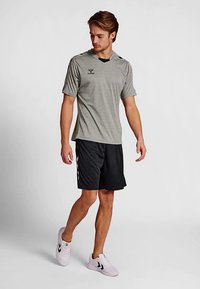 Camiseta deportiva gris de manga corta con detalles en negro, combinada con pantalones cortos negros. Zapatillas deportivas blancas con rayas negras.