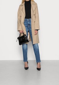 Beige trenchcoat över en svart polotröja, parat med blåjeans och svarta klackskor med spetsig tå. Svart handväska med krokodilstruktur.