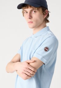 Svijetloplavi polo majica od teksturiranog materijala s klasičnim ovratnikom, s okruglom zakrpom logotipa Colmar na lijevom rukavu.