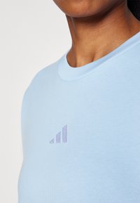 Lys blå bomull t-skjorte med rund hals og ribbestrikket detaljer, med et subtilt lilla logo-design på brystet.