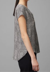 Blouse à manches courtes avec un motif noir et blanc, coupe décontractée, col en V, ourlet arrondi, tissu léger, texture lisse.