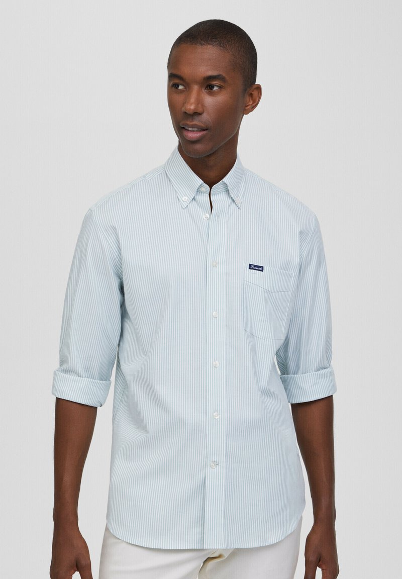 Camicia button-up a righe blu chiaro e bianche con maniche arrotolate, una tasca sul petto e una toppa con logo vicino alla tasca. Tessuto di cotone.