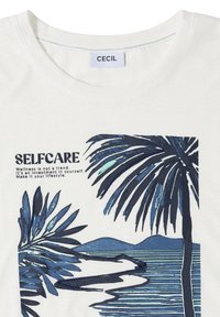 T-shirt blanc avec des palmiers bleus, des vagues de l'océan et le texte : « SELFCARE Le bien-être n'est pas une tendance. C’est un investissement en soi. »