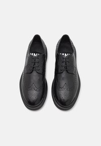 Scarpe in pelle nera con lacci, caratterizzate da un design brogue con dettagli perforati, punta arrotondata e suola robusta per garantire durabilità.