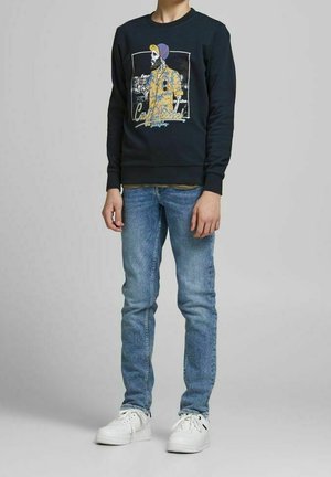 Sweat-shirt bleu marine avec impression graphique d'une silhouette, associé à un jean bleu clair et des baskets blanches. Tissu lisse, col rond, coupe ajustée.