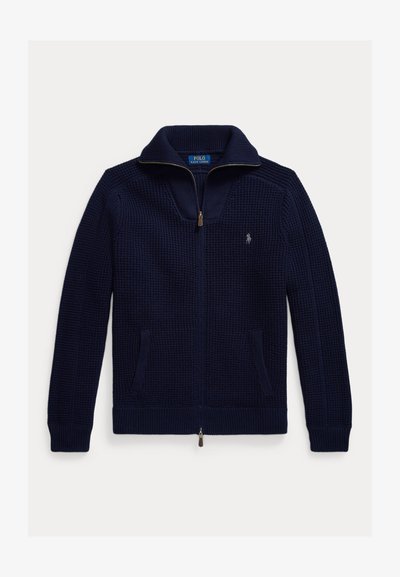 Navy zip-up sweater made of textured knit fabric. Features a high collar, two side pockets, and a small embroidered logo on the chest.