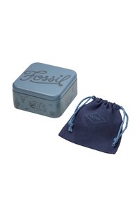 Boîte en métal carré bleu avec le texte "Fossil" en relief et des illustrations ; accompagnée d'un sac en satin bleu foncé avec un logo assorti.