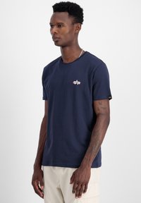 Dunkelblaues Baumwoll-T-Shirt mit einem kleinen gestickten Stern-Logo auf der Brust und einem umgeschlagenen Ärmel-Detail. Klassisches Rundhals-Design.