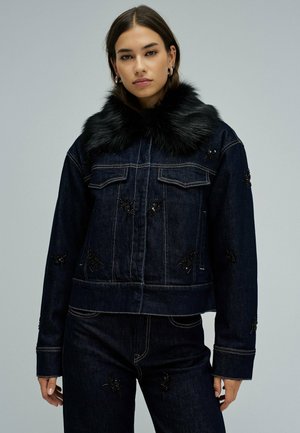 Veste en denim foncé avec un col en fausse fourrure noire, ornée de motifs floraux brodés et de poches avant. La veste a une silhouette courte.