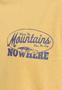 Κίτρινο ύφασμα με μπλε κείμενο που γράφει «Όπου τα βουνά φιλιούνται με τον ουρανό» και «ΠΟΥΘΕΝΑ» περιβάλλοντας μια γραφική εικόνα με vintage αυτοκίνητο.