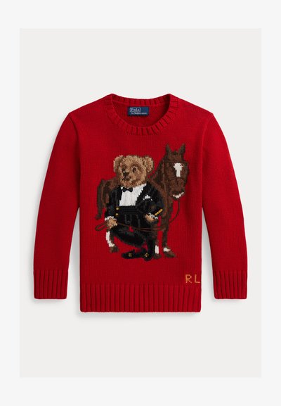 Rode gebreide trui met een beer in een smoking die teugels vasthoudt, staand naast een bruin paard met een witte bles op zijn gezicht.