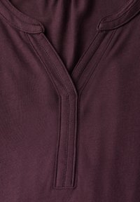 Burgundská oděv s výstřihem do V a kontrastním švem. Hladká textura, lehká tkanina a jemné podrobnosti švů.