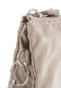 Brun stofpose med en tekstureret finish, der har en sølvfarvet lynlås og metalring hardware fastgjort til siden.