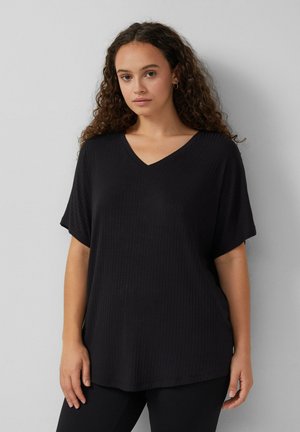Haut noir à manches courtes et col en V, avec un tissu côtelé. Coupe loose avec un tissu texturé. Porté avec un bas noir, complétant le style décontracté.